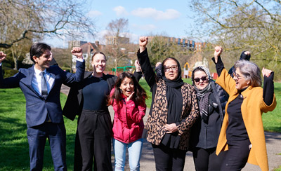 Group of diverse individuals celebrating joyfully in a park, raising their arms in a show of community and support.